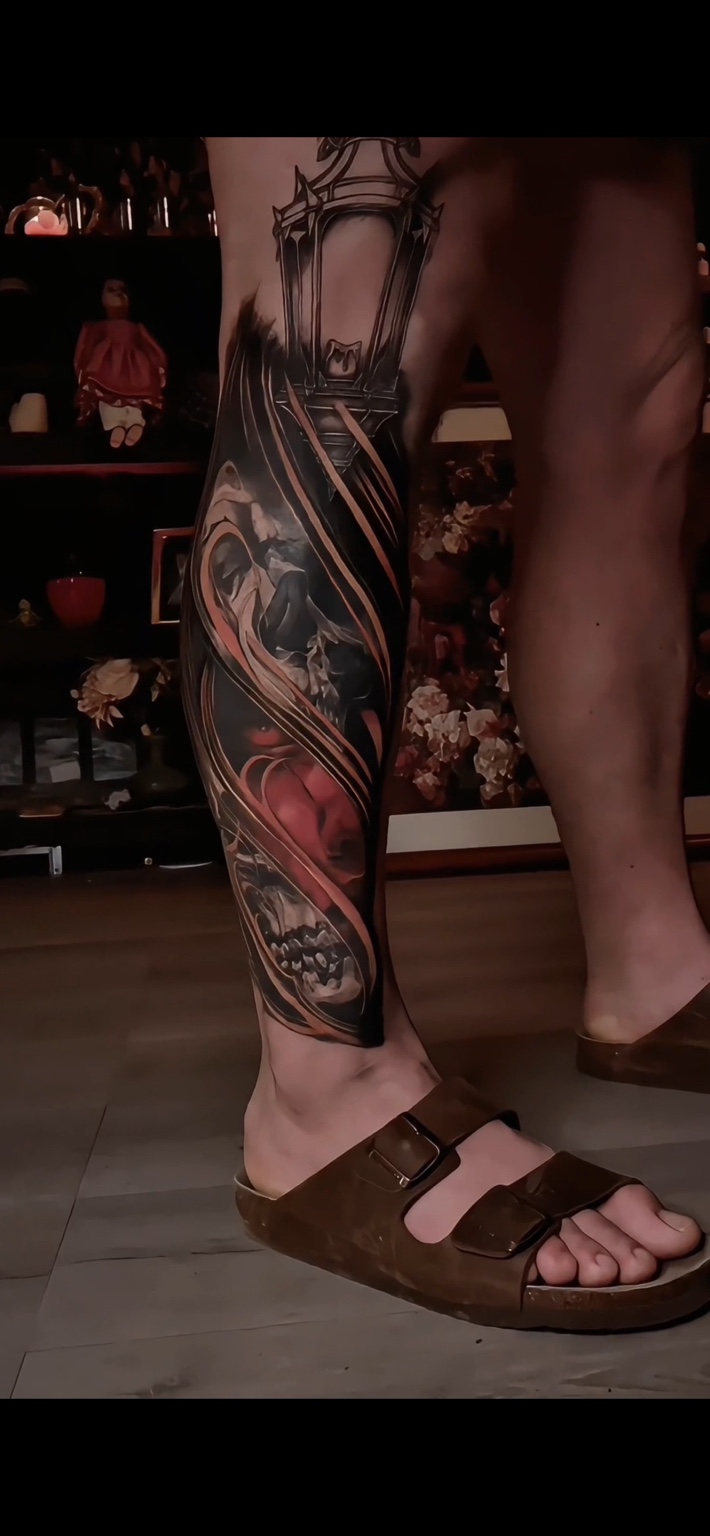 Black and grey leg tattoo with gothic architecture, skulls and flowing red details
